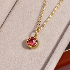 Macro shot of gold necklace with round red faceted gemstone pendant in bezel setting