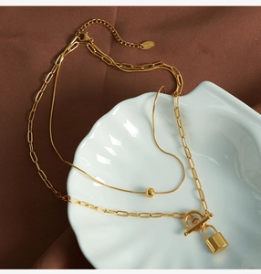 Detailed view of golden double-layer necklace with padlock pendant and OT buckle toggle