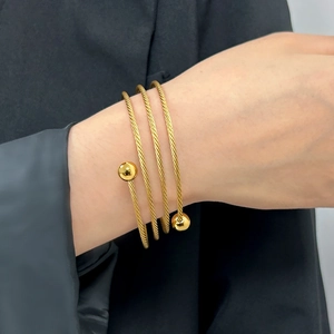 Dettaglio di un bracciale a cavo dorato multistrato con accenti di sfere metalliche