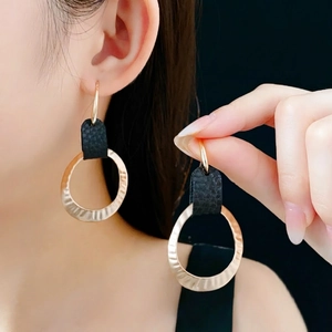 Fashionable textured gold hoop earrings with black leather accents on a female model