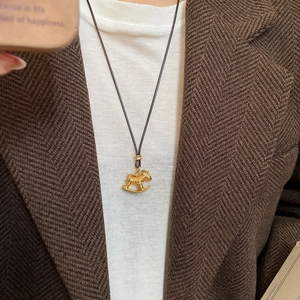 Close-up of golden rocking horse pendant with leather cord worn on an autumn outfit
