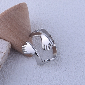 Macro shot of silver hugging arms open ring showing detailed hand clasp on textured stone