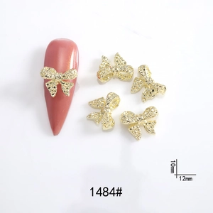 Detail of 10mm and 12mm gold metal 3D bowknot nail charms on pink manicure nails