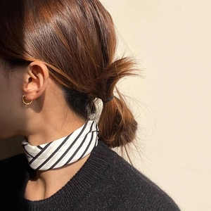 Close-up of minimalist gold oval earrings worn by model with striped silk scarf