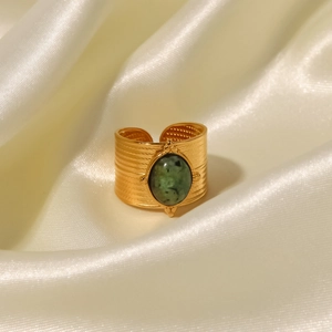 Detail of 18K gold wide band ring with green gemstone on smooth white silk fabric