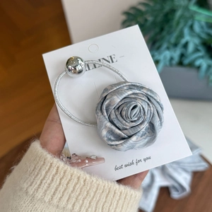 Light blue floral rose hair tie with silver bead on card held by a hand