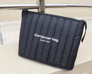 Black vertical quilted laptop sleeve with top zipper and woven handle on stone base