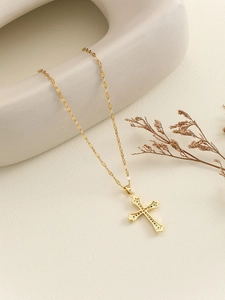 Close-up of golden cross necklace with colorful zircons on minimalist ceramic decor