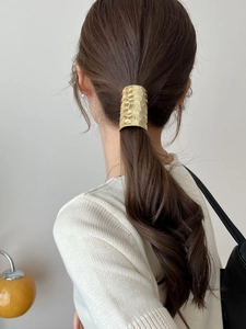 Detailed view of golden hammered metal hair cuff accessory on a sleek ponytail