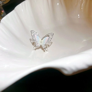 Detailed macro view of an iridescent butterfly ring with crystal accents on a shell tray
