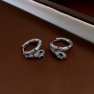 Silver snake hoop earrings with white zircon pavé and black gems on a brown background