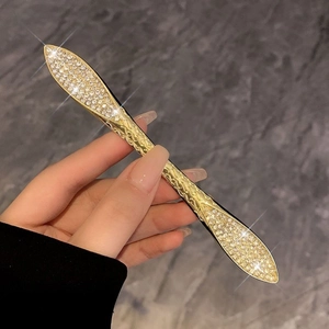 Detail of a vintage golden hair pin with rhinestones held against a grey background