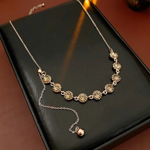 Detailed macro view of vintage gold necklace with green rhinestones and a small bell pendant