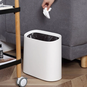 Minimalist white plastic oval trash can placed by a sofa in a modern home interior