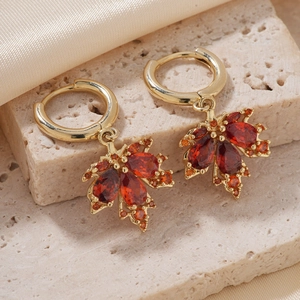 Elegant gold maple leaf stud earrings with red and orange zircon on textured stone and silk