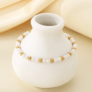 Detailansicht eines Perlen- und Goldperlenarmbands an einer weißen Porzellanvase