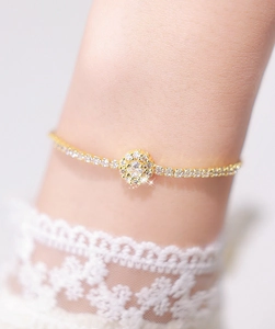 Close-up of a gold chain bracelet featuring a zircon flower charm on a woman's wrist