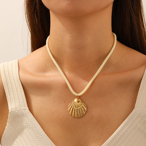 Détail d'un pendentif coquillage doré sur cordon tressé blanc porté par un modèle