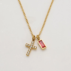 Close-up of gold cross necklace featuring clear zircon and red rectangular gemstone