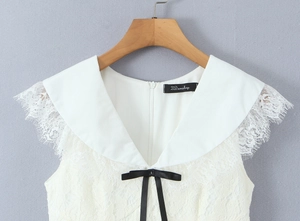 Detail of white lace dress featuring a navy collar with a black satin bow and zip closure