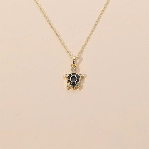 Gold plated turtle necklace with black enamel and zircons on a beige background