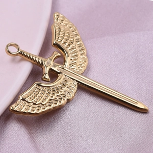 Gold stainless steel wing and sword pendant on soft pink fabric background