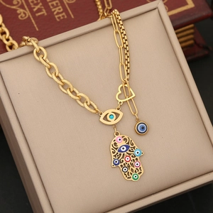 Detailed view of golden Hamsa hand and evil eye charms on layered chains in a jewelry box