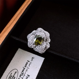 Macro shot of silver camellia flower ring with green gem and pavé diamond details