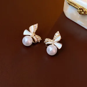 Elegant gold bow earrings with zircon stones and round white pearls on a leather base