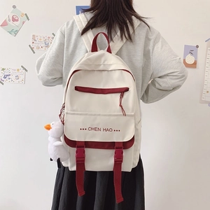 Student backpack detail showing cream canvas with red trim and a cute duck plush charm