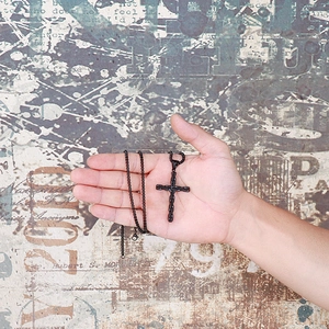 Dettaglio di una mano che tiene un ciondolo a croce in acciaio inossidabile nero su catena box