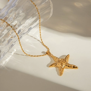18k gold plated stainless steel starfish pendant necklace on a decorative glass