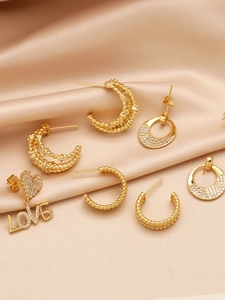 Detailed view of gold C-shape twisted earrings and heart LOVE charms on silk fabric