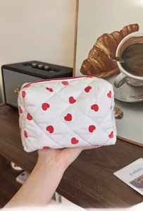 Detail of white quilted cotton cosmetic bag featuring red heart patterns and zip closure
