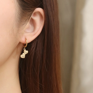 Detailed macro view of gold hoop earrings featuring double textured heart pendants with gems