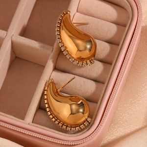 Détail de boucles d'oreilles goutte d'or avec cristaux sur un écrin rose poudré