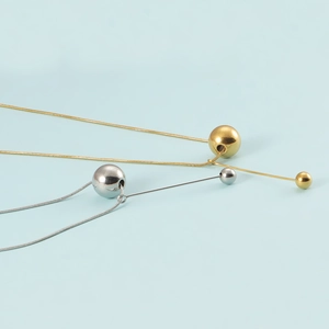 Detailed close-up of gold and silver ball pendant necklaces with snake chains on blue