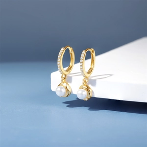 Macro view of gold pearl hoop earrings with white zircon accents on blue background