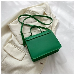 Green square crossbody bag in PU leather with chain strap on a beige blazer