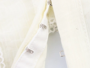 Close-up of metal hook-and-eye closures on a cream puffed sleeve blouse texture