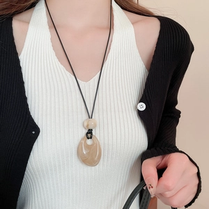Fashionable black cord necklace with beige teardrop resin pendant worn by model