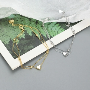 Detail of layered S925 silver bracelets with heart charms in gold and silver finishes