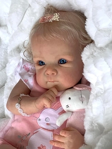Close-up of realistic newborn doll with blonde curls, blue eyes, and pink rabbit dress