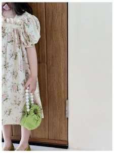 Close-up of floral girls dress with puff sleeves and green pearl handle handbag