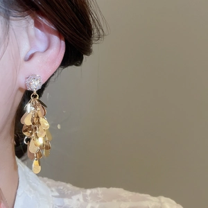 Close-up of gold layered teardrop fringe earrings worn by a model in a luxury setting