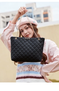 Détail du sac cabas matelassé noir avec chaîne dorée porté par un mannequin élégant