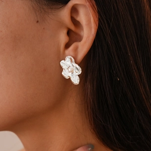 Detail of silver flower stud earring with hammered metal texture and center pearl on model