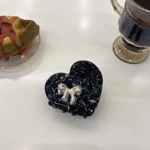 Macro detail of heart-shaped marble acetate hair claw with white ribbon on white desk
