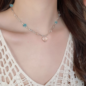 Detail of light blue glass beaded necklace with a silver heart pendant on a female model