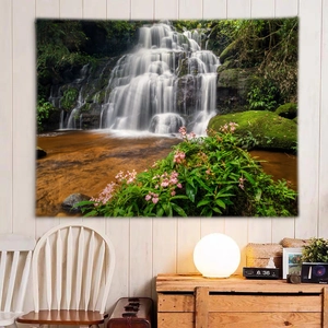 Detailed nature forest waterfall wall tapestry hanging above a wooden cabinet and cozy lamp